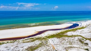 An aerial view of a beach with a clear blue sky, a sandy shoreline, and a distinct water body with a dark area. - 30A | Gorgeous Home | Resort Pool (Rosemary Beach)
