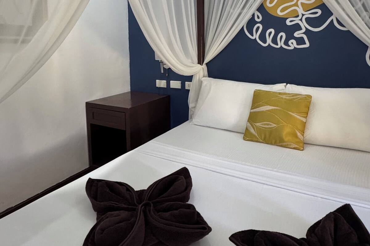 Ein Hotelzimmer mit einem Bett, weißen Vorhängen, einem Nachttisch und einer Wand mit Dekoration.