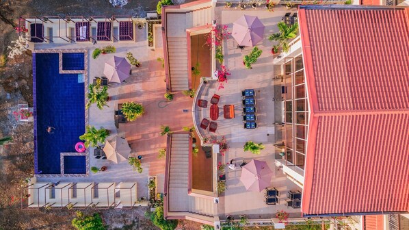 Vista aérea de un hotel con piscina, zonas de estar al aire libre y un edificio de techo rojo.