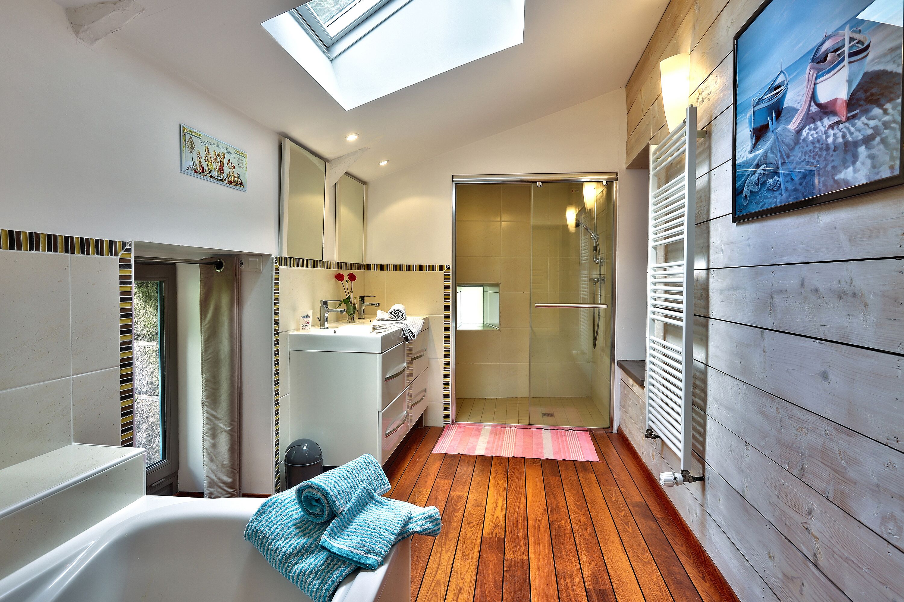 Een moderne badkamer met dakraam, ligbad, douche en een houten vloer.