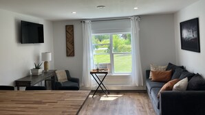 Ett modernt vardagsrum med ett stort fönster, en platt-TV, en soffa och en matplats.