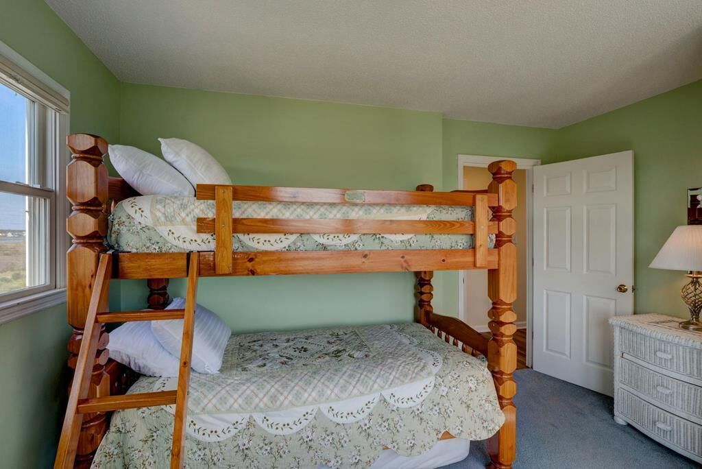 A bunk bed with a ladder, a white dresser, and a door in a room with green walls.