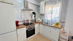 Una cocina moderna con armarios blancos, horno empotrado, microondas y cafetera.