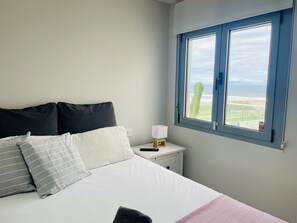 A bedroom with a bed, pillows, a bedside table with a lamp, and a window with a view.
