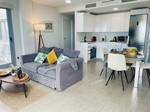 A modern living room with a grey sofa, a small round table, and a dining area with a glass table and chairs. - Dunas Beach Penthouse (Torrox Costa)