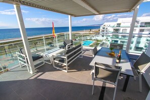 A balcony with outdoor furniture, a table with a bottle and glasses, and a view of the sea and buildings.