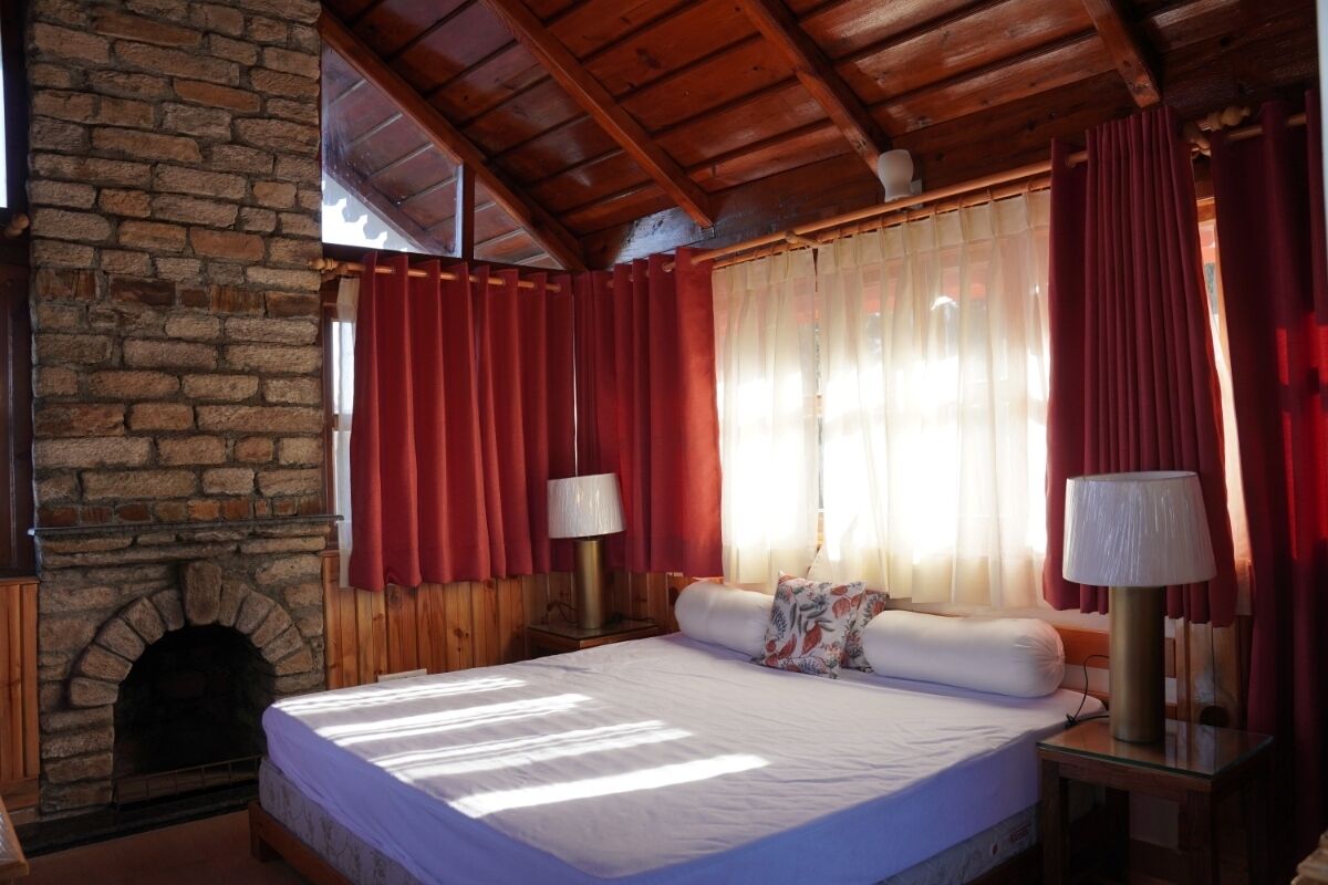 A bedroom with a stone fireplace, wooden ceiling, and a bed with red curtains.