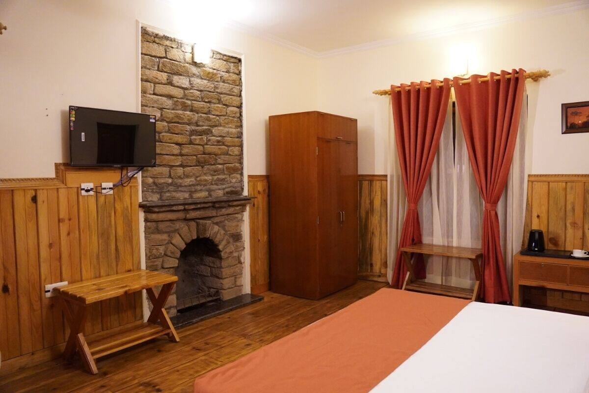A room with a stone fireplace, wooden wardrobe, a television mounted on the wall, and a bed with an orange bedspread.