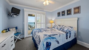 A bedroom with a bed, a desk, a chair, a TV, and a view of the ocean through a door. - A Southern Charm - 5BR Oceanfront House in Surf City Sleeps 12 (Surf City)