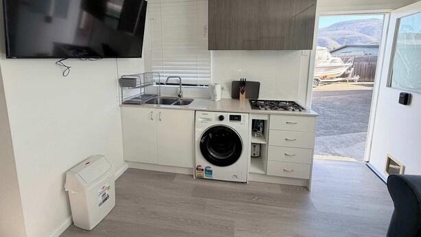 A compact kitchenette with a washing machine, a sink, and a stove. - Private Studio | Convenient Stay Near Hobart (Claremont)