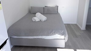 A neatly made bed with grey bedding, a white pillow, and a rolled white towel. - Private Studio | Convenient Stay Near Hobart (Claremont)