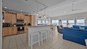 Una cocina moderna con una isla central, taburetes de bar blancos y una zona de comedor con sofá azul.