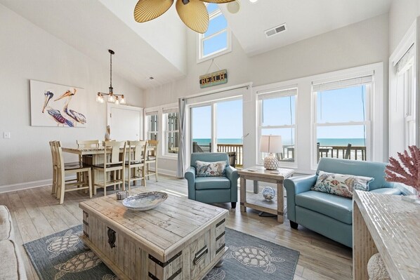 A spacious living room with a dining area, large windows, and a view of the beach. - 4 Bedroom Oceanfront Townhome in North Topsail - Sleeps 12 (North Topsail Beach)