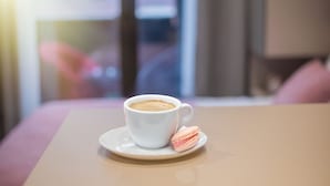 Eine Tasse Kaffee auf einem Untertasse mit einem rosa Macaron daneben auf einem Tisch.