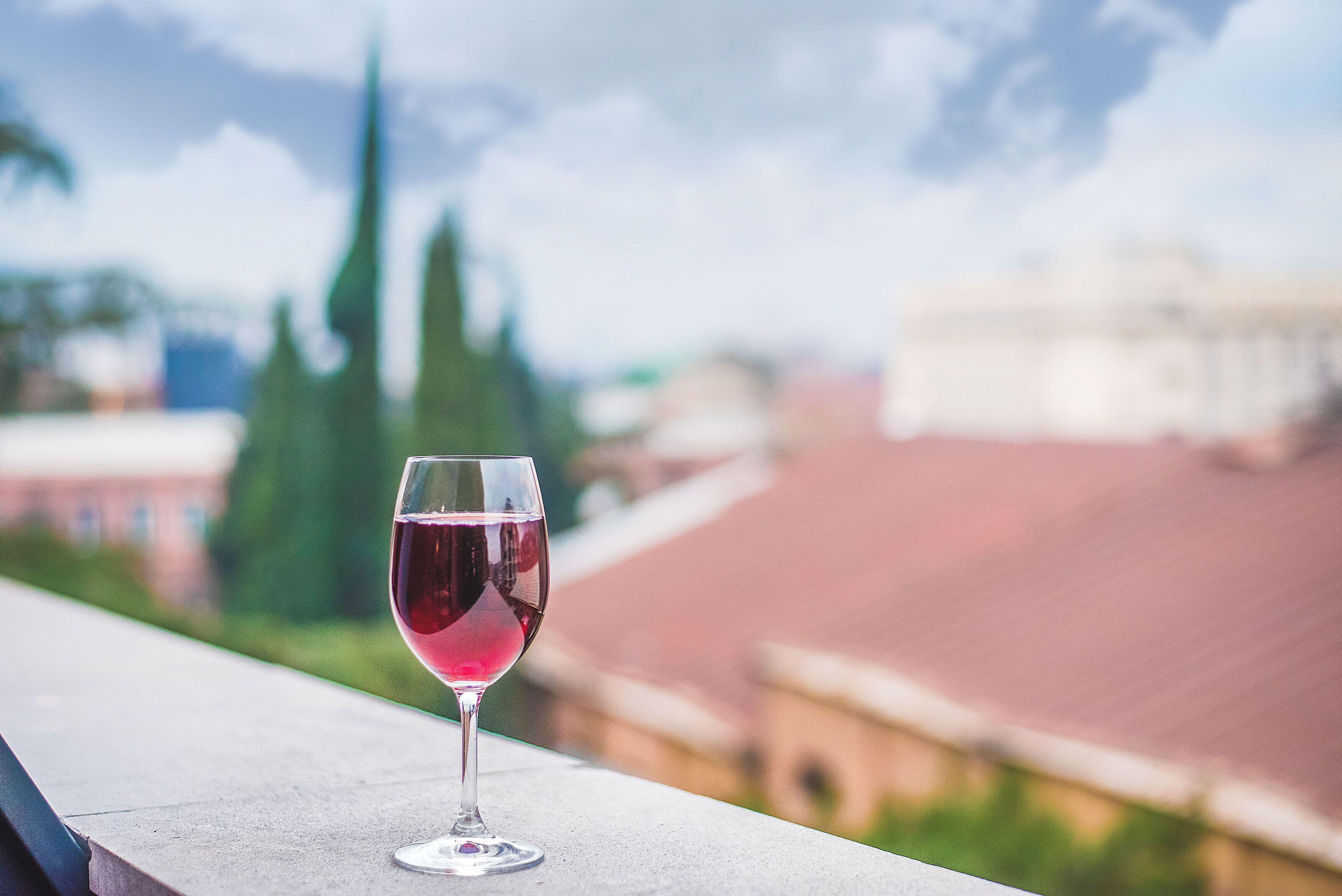 A glass of red wine on a balcony with a blurred cityscape in the background.