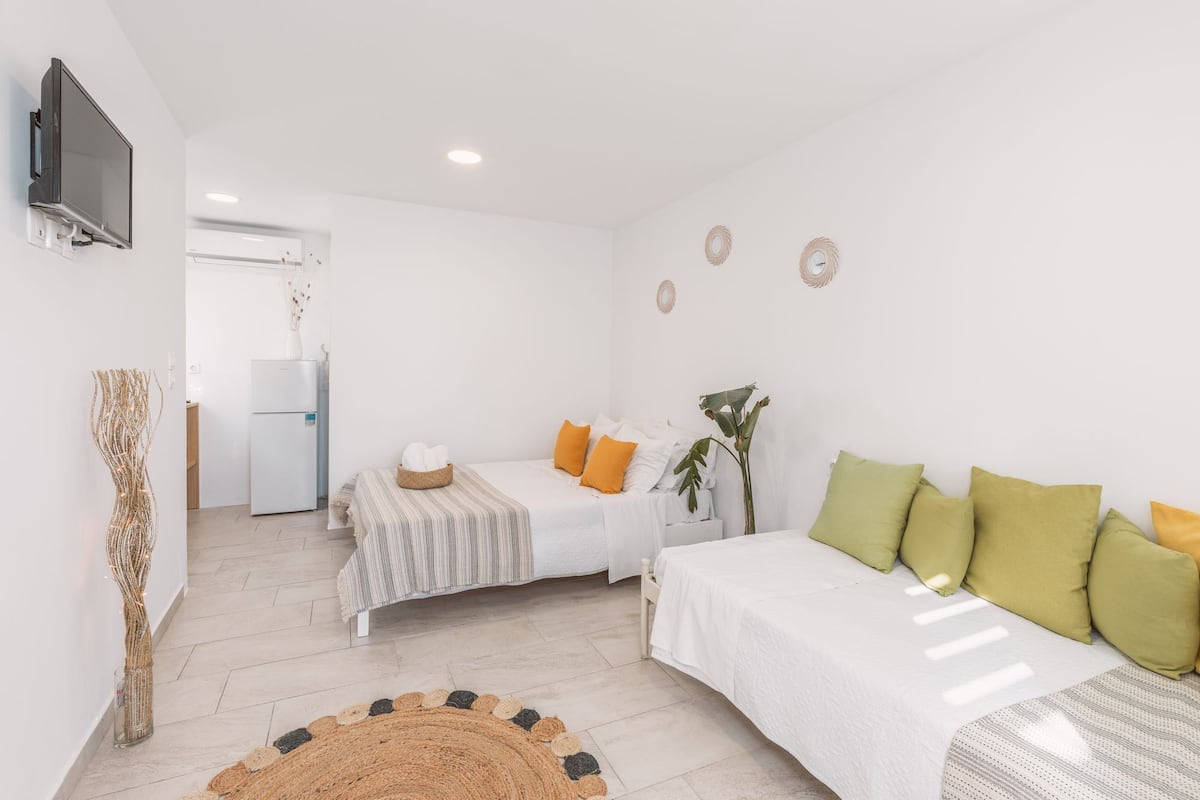 Une chambre à coucher moderne et minimaliste, avec deux lits, une télévision et une cuisine en arrière-plan.