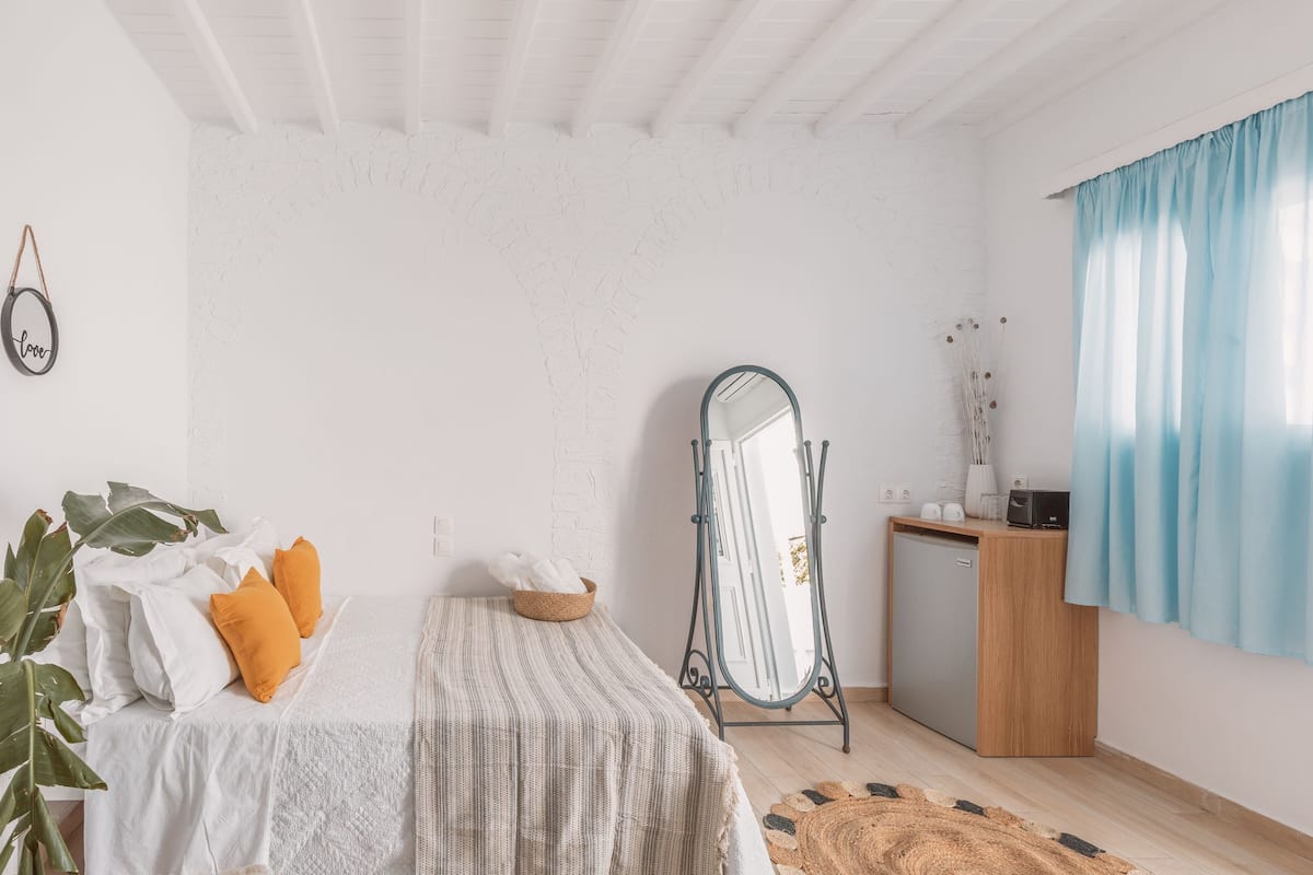 Une chambre à coucher avec un lit, une commode, un miroir et une fenêtre avec des rideaux.