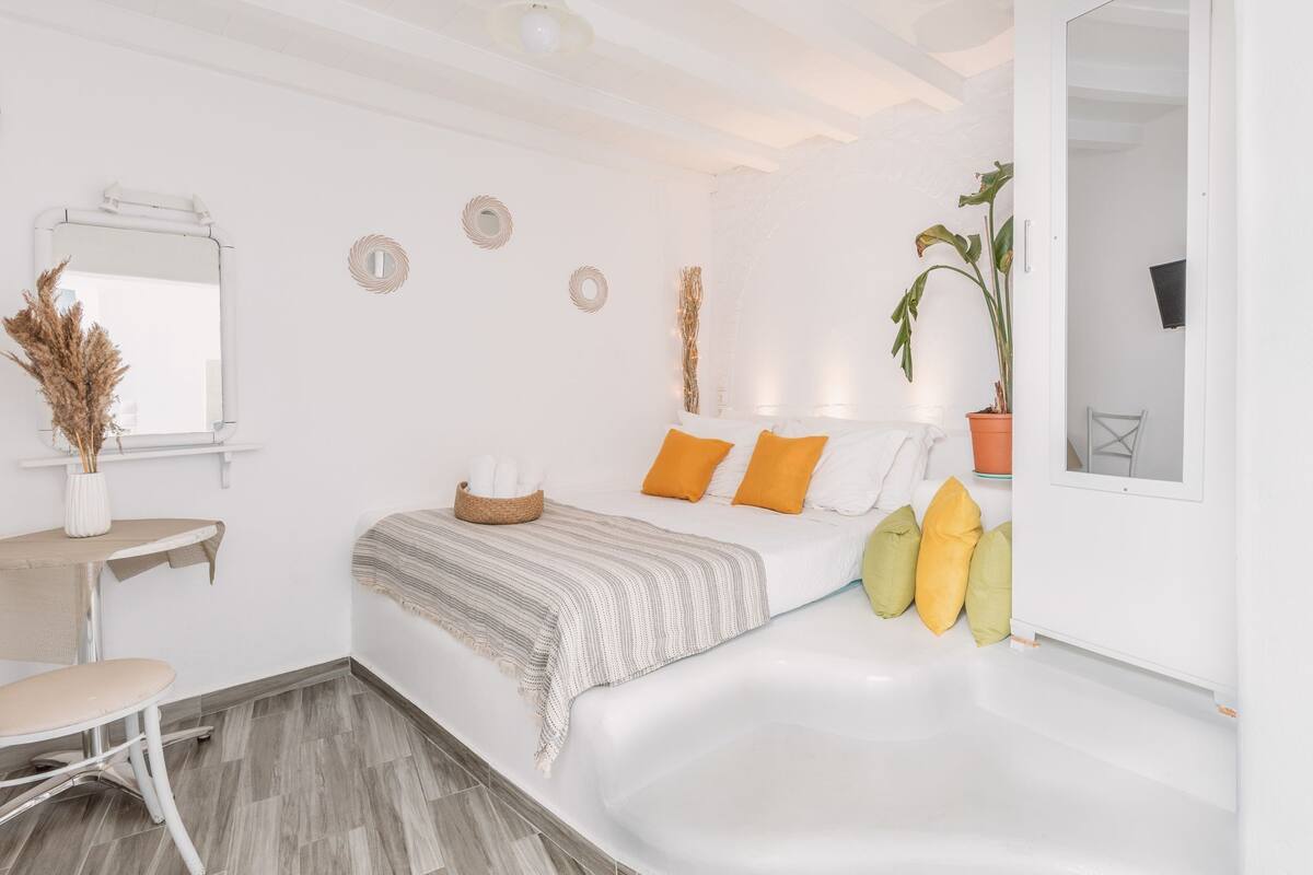 Une chambre moderne avec un grand lit, une petite table de chevet, une chaise, une fenêtre et une salle de bain avec une baignoire.