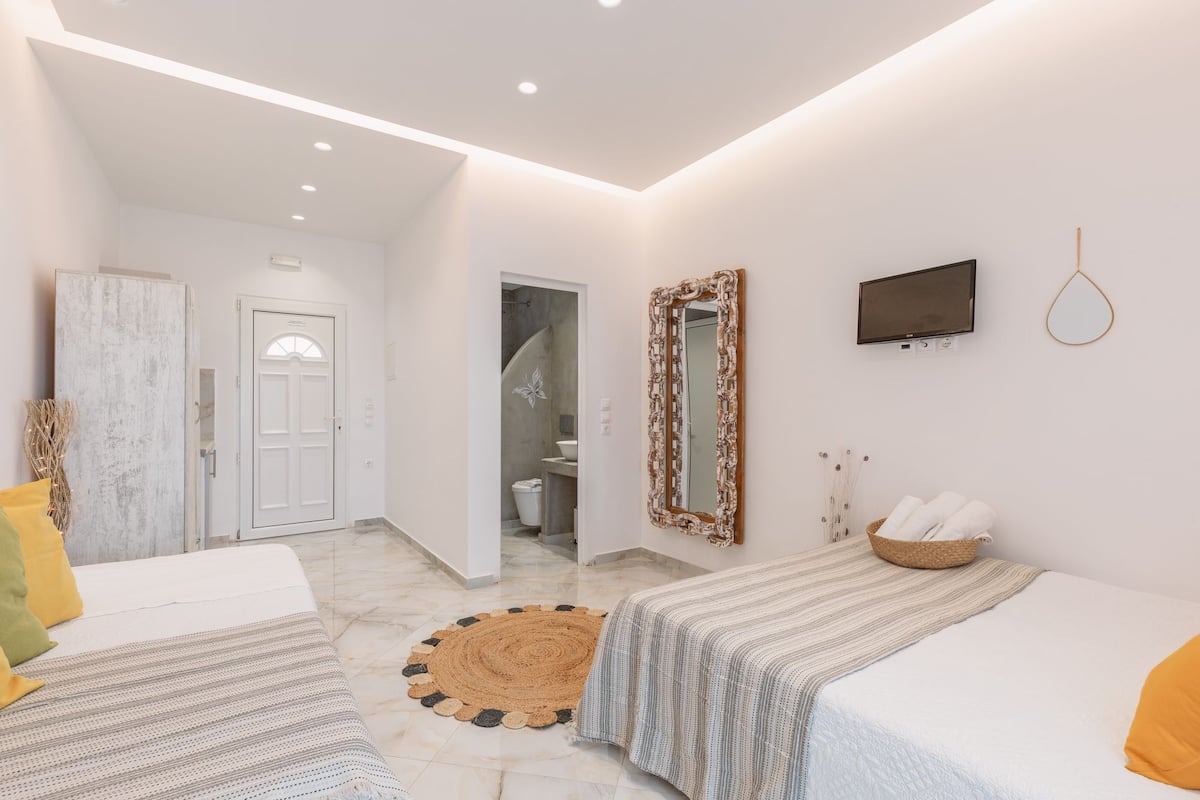 Une chambre moderne avec un grand lit, un plus petit lit, une télévision et un miroir.