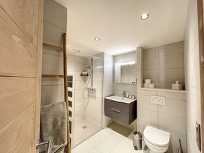 Une salle de bain moderne avec une douche à parois de verre, une porte en bois, un lavabo blanc et des toilettes.