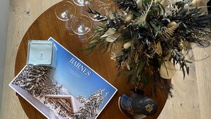 Una mesa redonda de madera con una revista, un candelabro de vidrio, una planta decorativa y tres copas de vino.