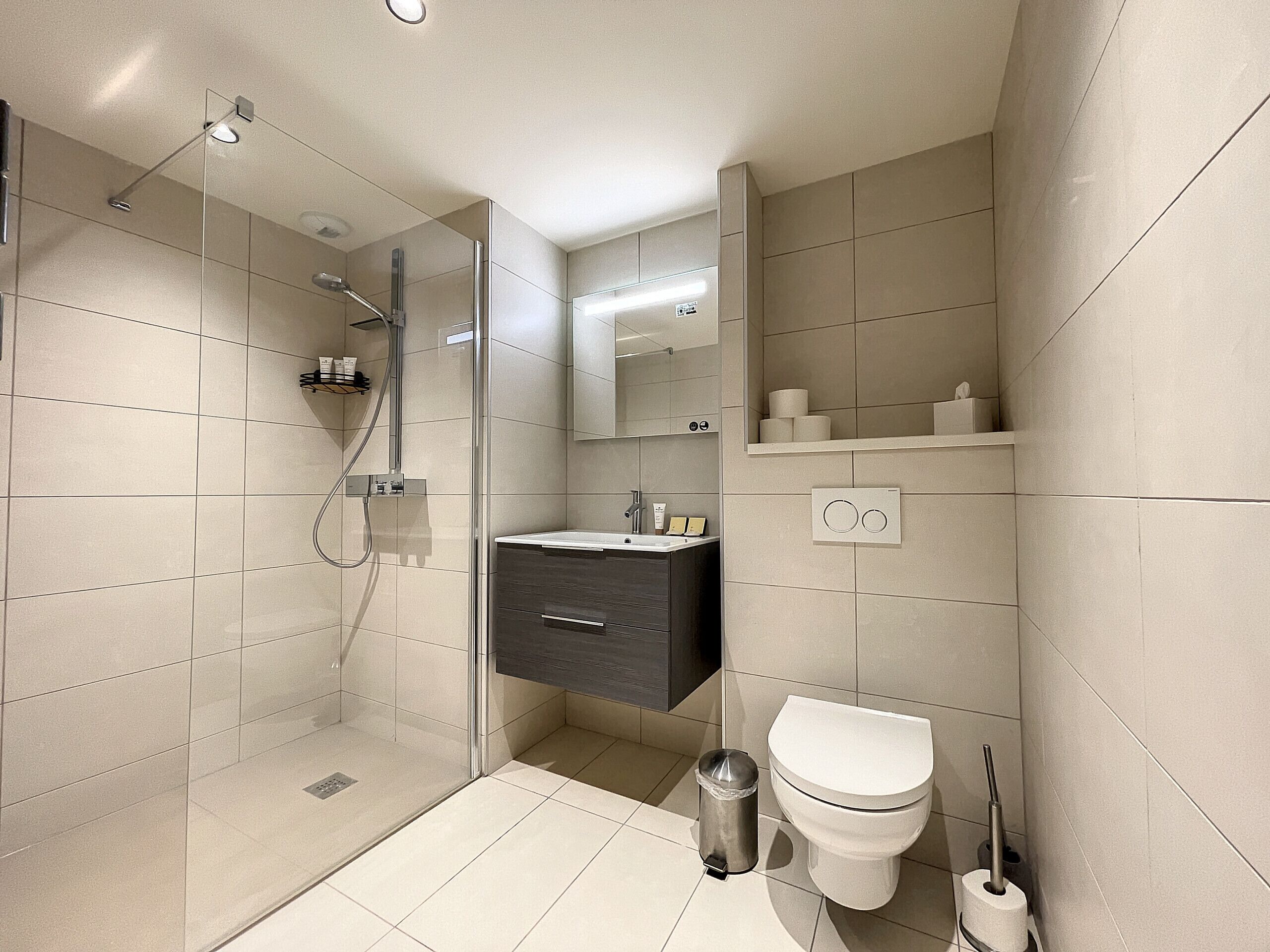 Un bagno moderno con doccia vetrata, un mobile lavabo con lavandino, un WC e uno specchio sopra il lavandino.