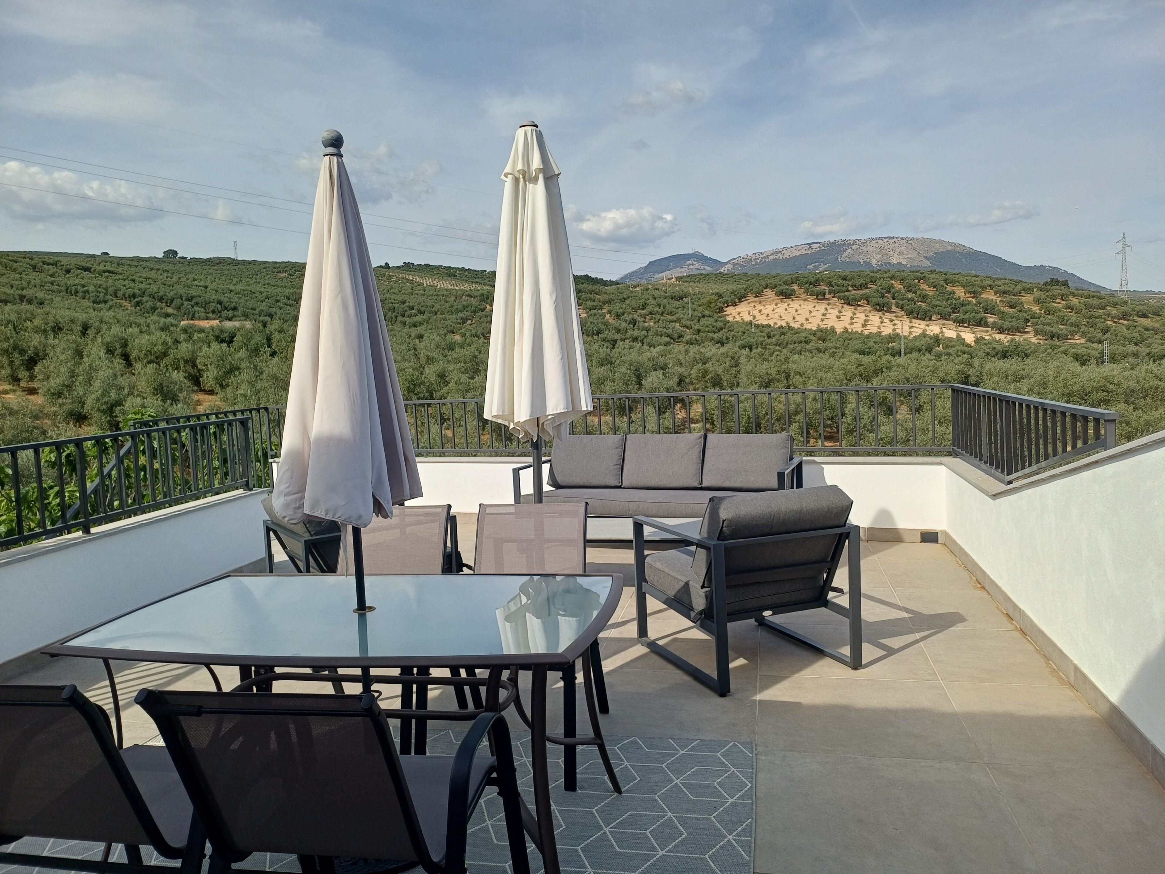 Un espace extérieur aménagé avec une table et des chaises, deux parasols et une vue sur un paysage vallonné.