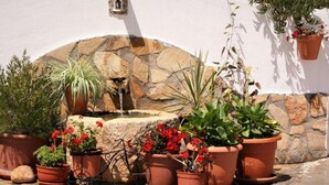 A stone wall with a small fountain, surrounded by potted plants and flowers. - Casita of Casa Olivar (Tocón)