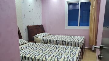 A bedroom with two beds, a window, and a door.