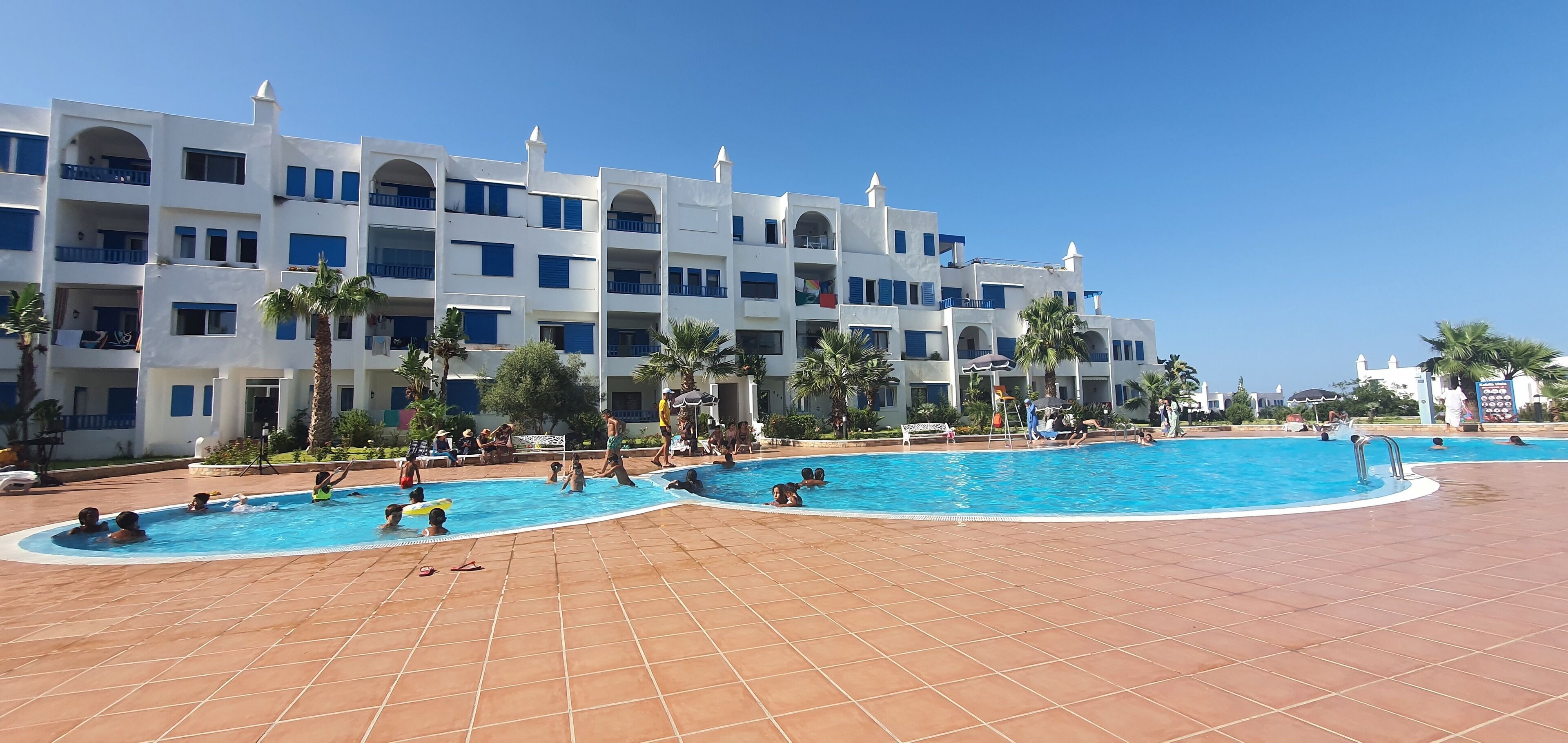A hotel with multiple swimming pools, palm trees, and a tiled patio area.