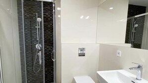 Un baño moderno con ducha de vidrio, inodoro y lavamanos con espejo.