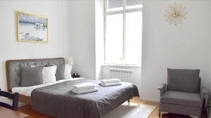 Un dormitorio con una cama, una silla, un ventanal y un cuadro en la pared.