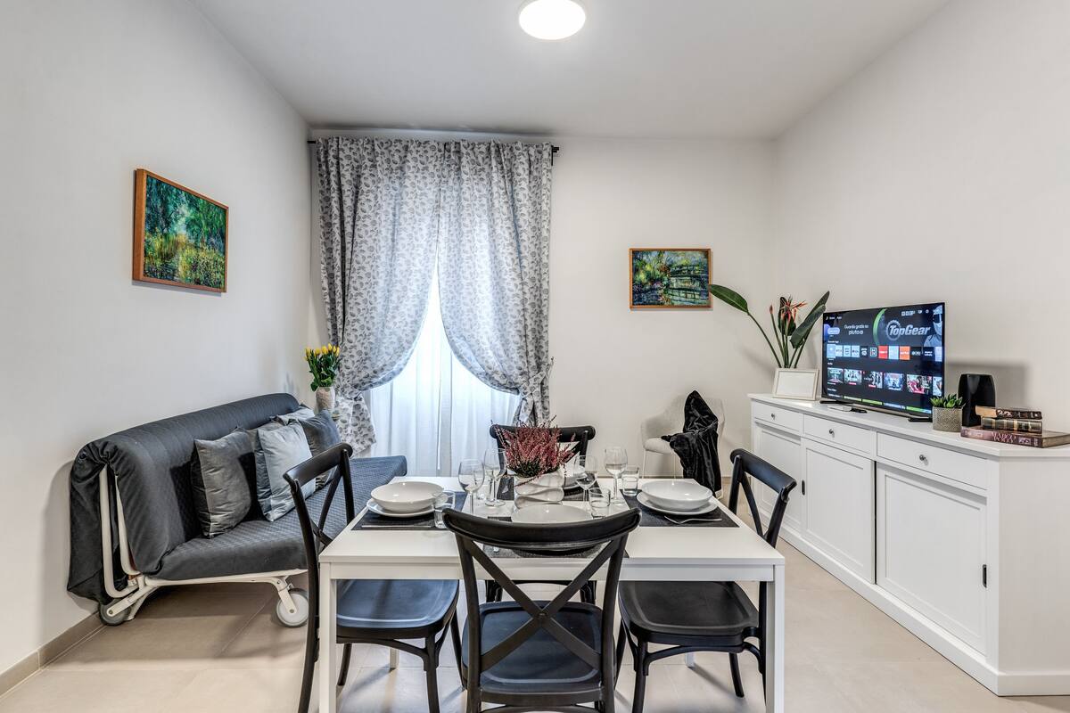 A dining area with a white table, black chairs, and a TV on a cabinet.