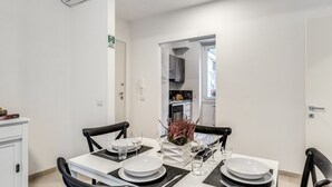 A dining area with a white table set for four, black chairs, and a small decorative plant. - Inn 3 (Rome)