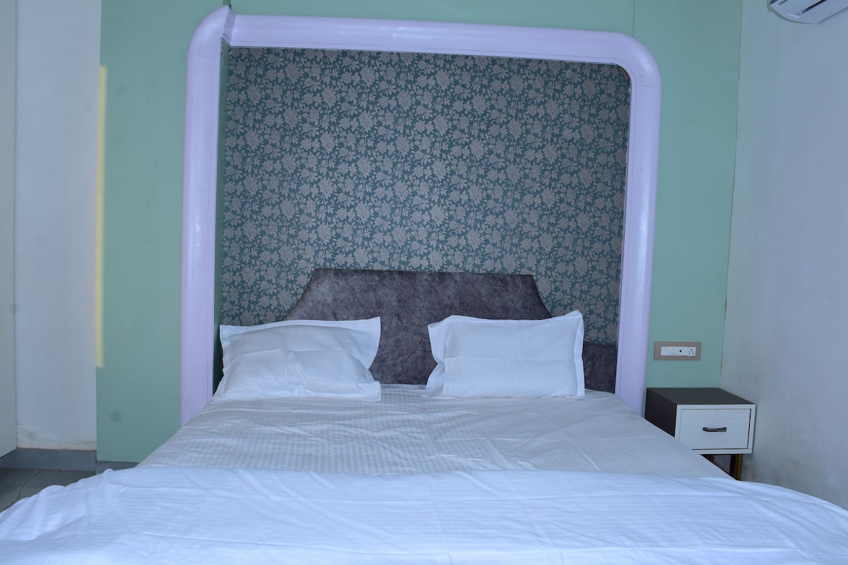 Ein Bett mit weißer Bettwäsche, ein Kopfteil mit floralem Muster und ein kleiner Nachttisch mit Schublade.
