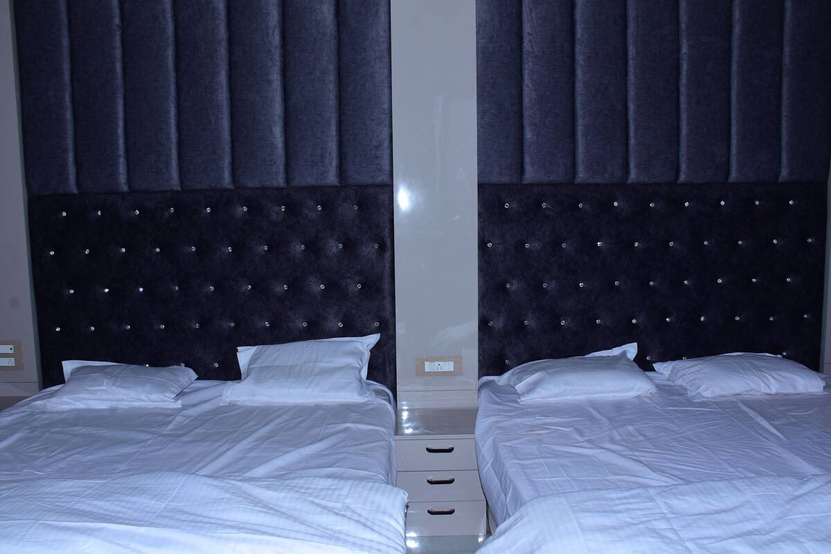 Ein Zimmer mit Spiegel und zwei Betten, jeweils mit weißer Bettwäsche und einem gepolsterten Kopfteil.