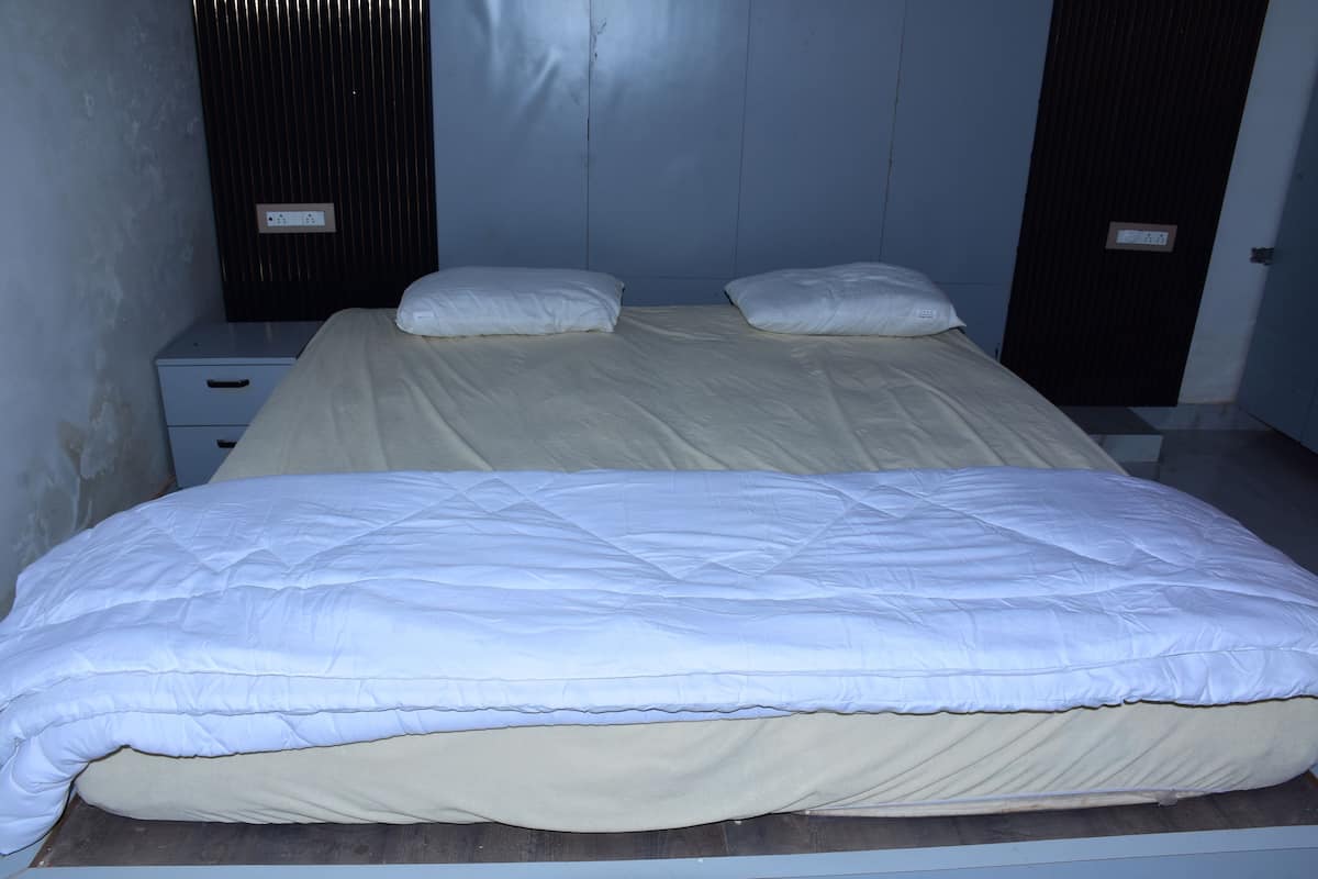 Ein Doppelbett mit beige-weiß gestreifter Bettdecke, ein Nachttisch mit Schublade und eine Wandsteckdose.