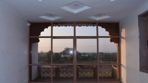 A room with a large glass door with intricate wooden carvings, a ceiling with recessed lighting, and a view of trees and power lines outside. - Rajrani Heritage Resort (Asind)