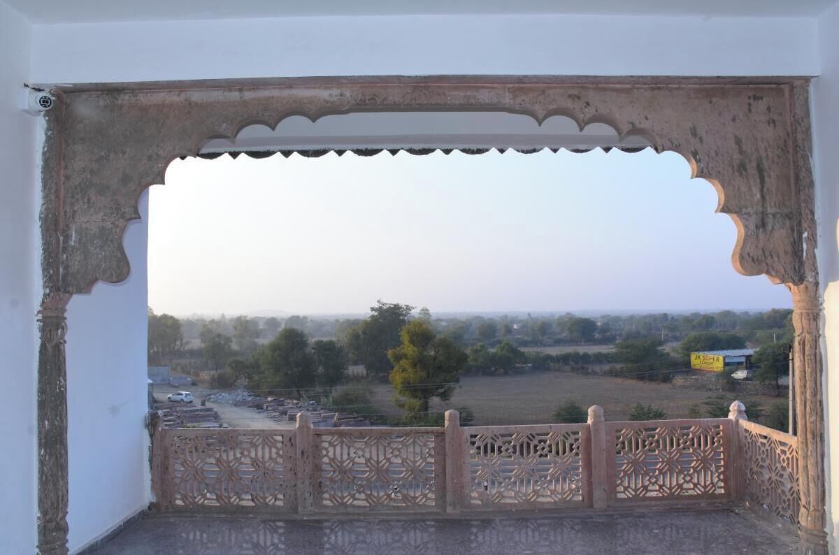 Vista a través de un puerta decorativa con barandilla ornamentada, mostrando un paisaje rural con campos y árboles.