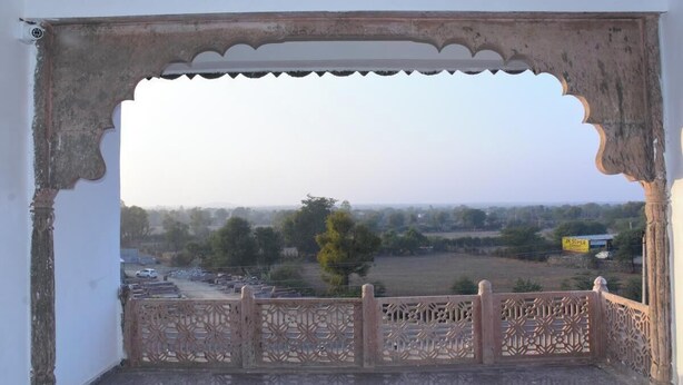 A view through an ornate doorway with a decorative railing, overlooking a rural landscape with fields and trees. - Rajrani Heritage Resort (Asind)