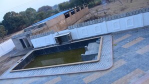 A courtyard with a decorative pool, a white wall with a patterned base, and a blue-roofed building in the background. - Rajrani Heritage Resort (Asind)