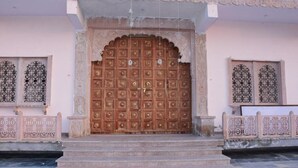 A large, ornate wooden door with intricate carvings, flanked by two windows with decorative grills. - Rajrani Heritage Resort (Asind)