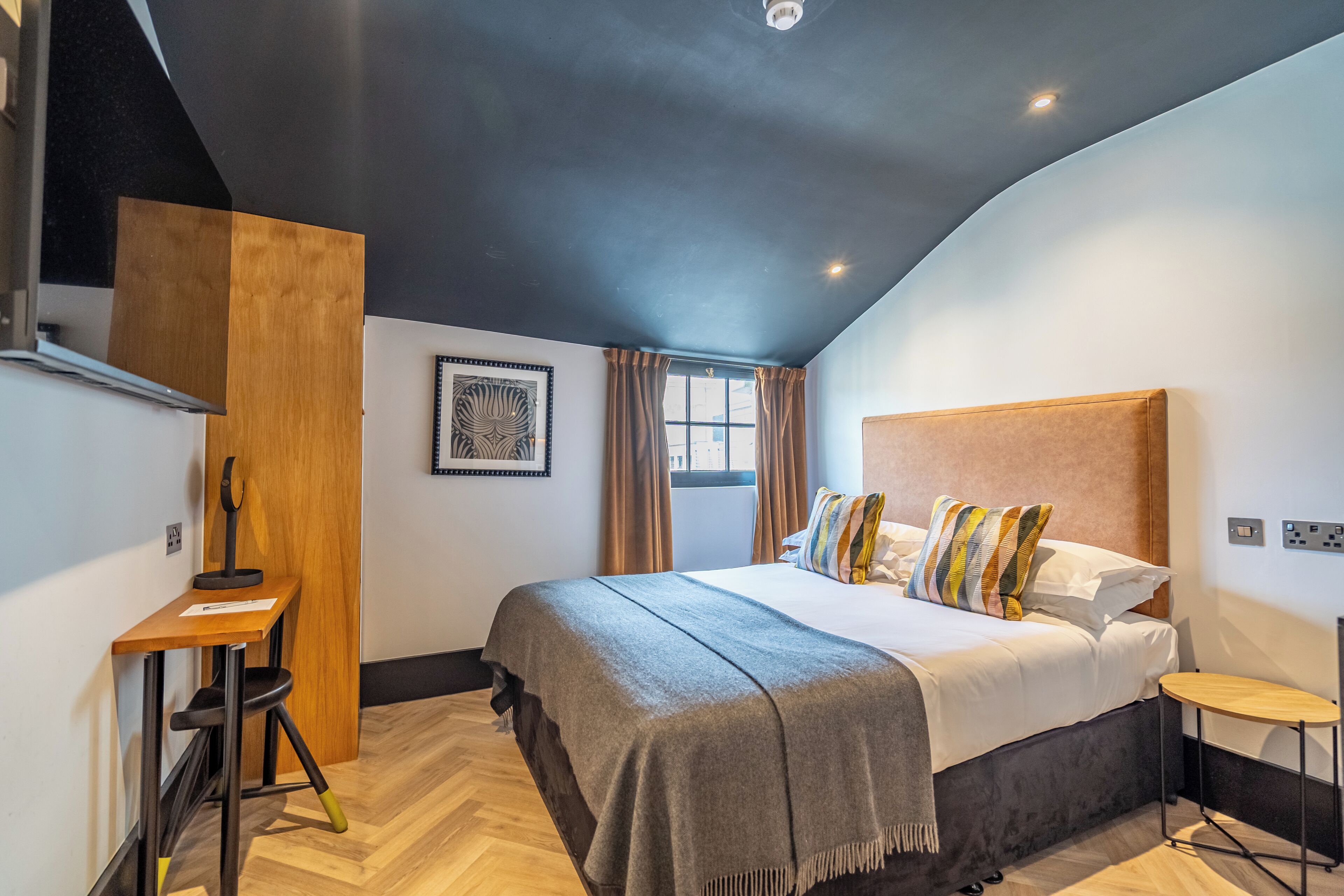 A modern bedroom with a large bed, a desk, and a window with curtains.