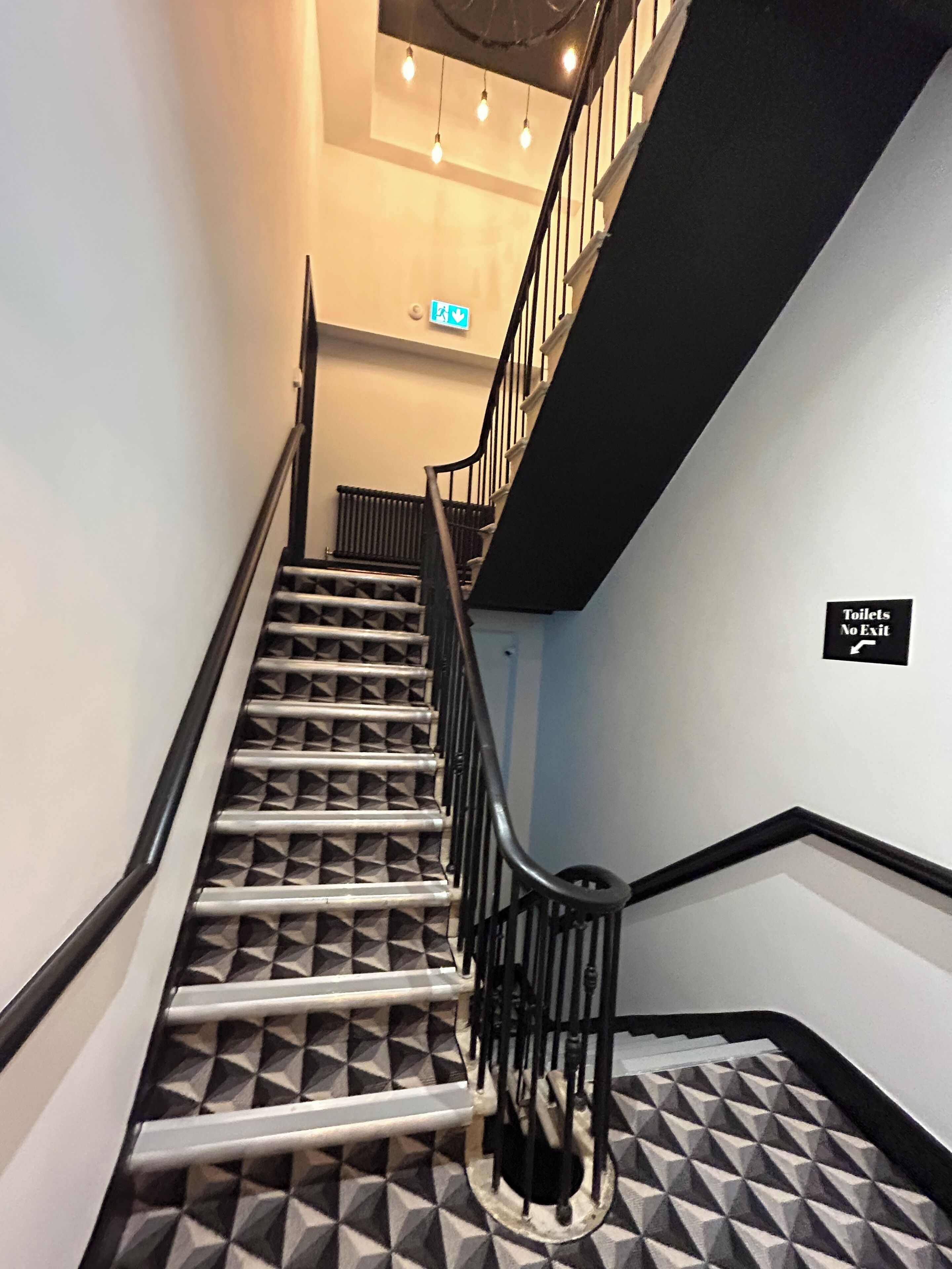 Eine Treppe mit geometrischem Fußbodenmuster und schwarzen Geländern.