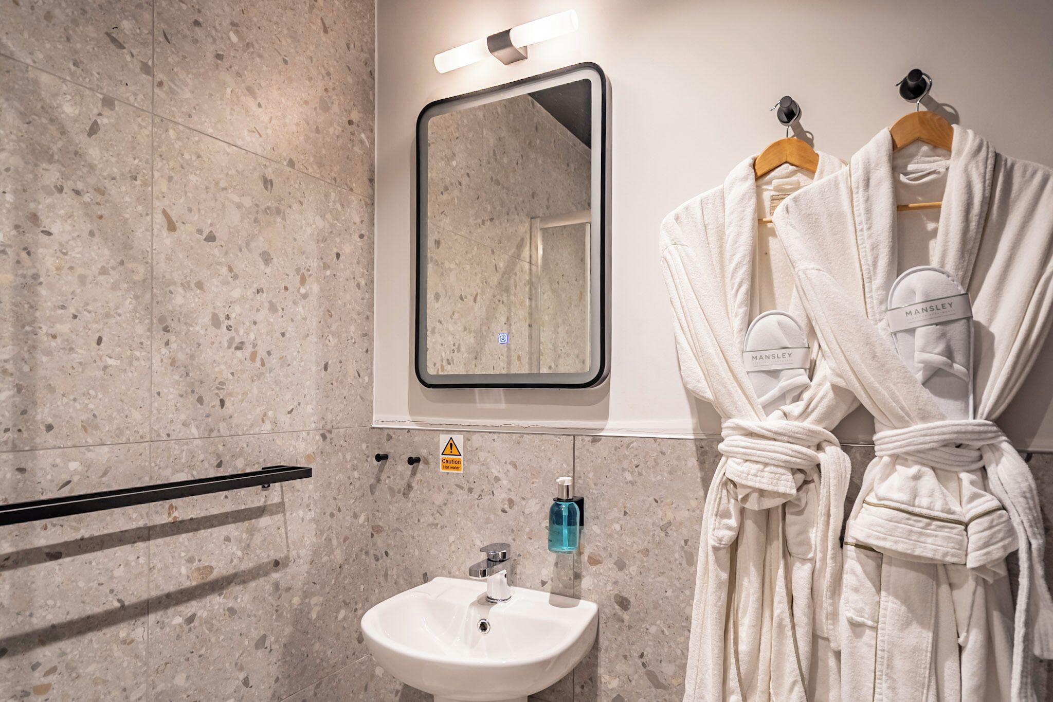 Une salle de bain avec un lavabo, un miroir et deux peignoirs suspendus à un porte-serviettes.