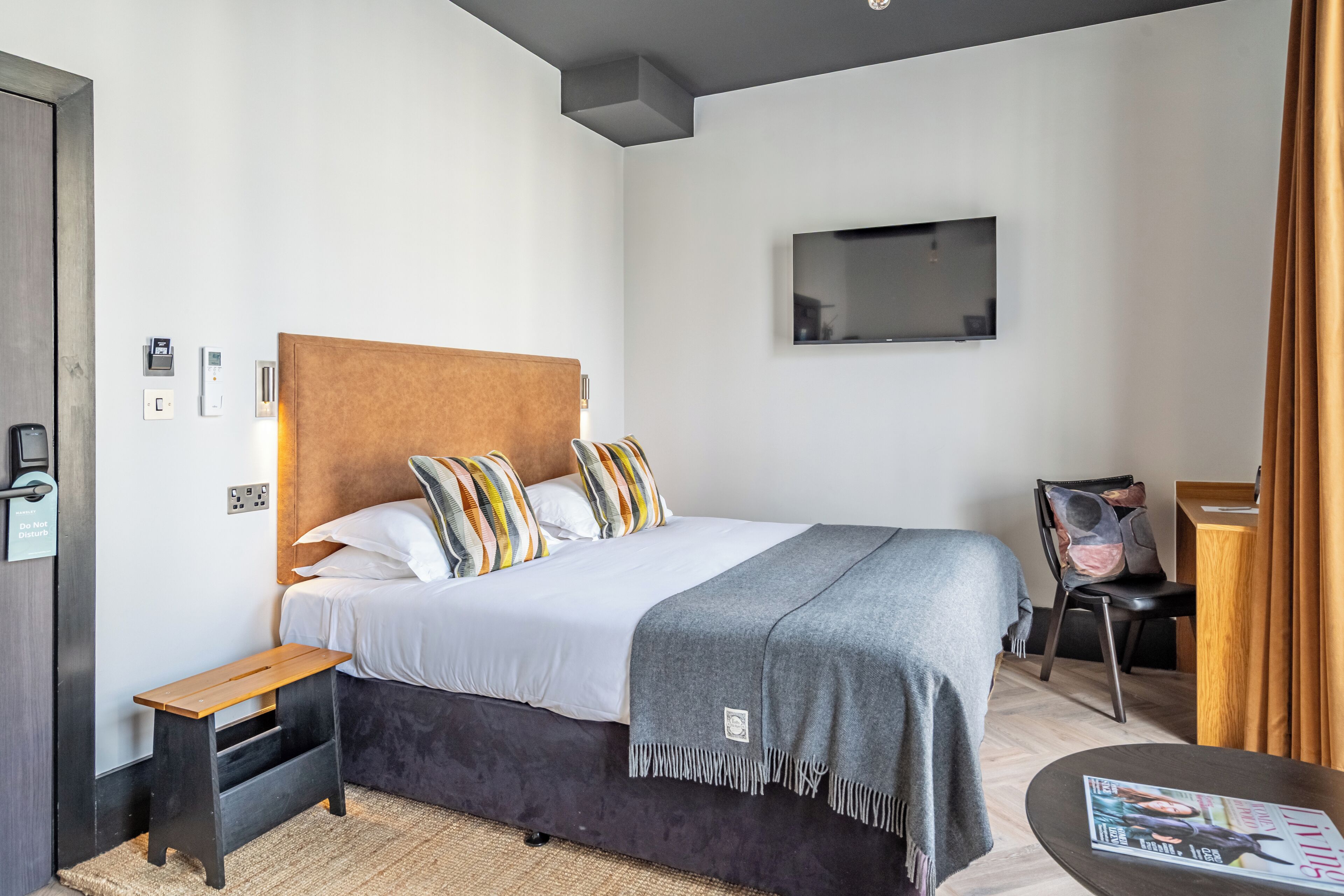A modern hotel room with a large bed, a bedside table, a small desk, and a television on the wall.