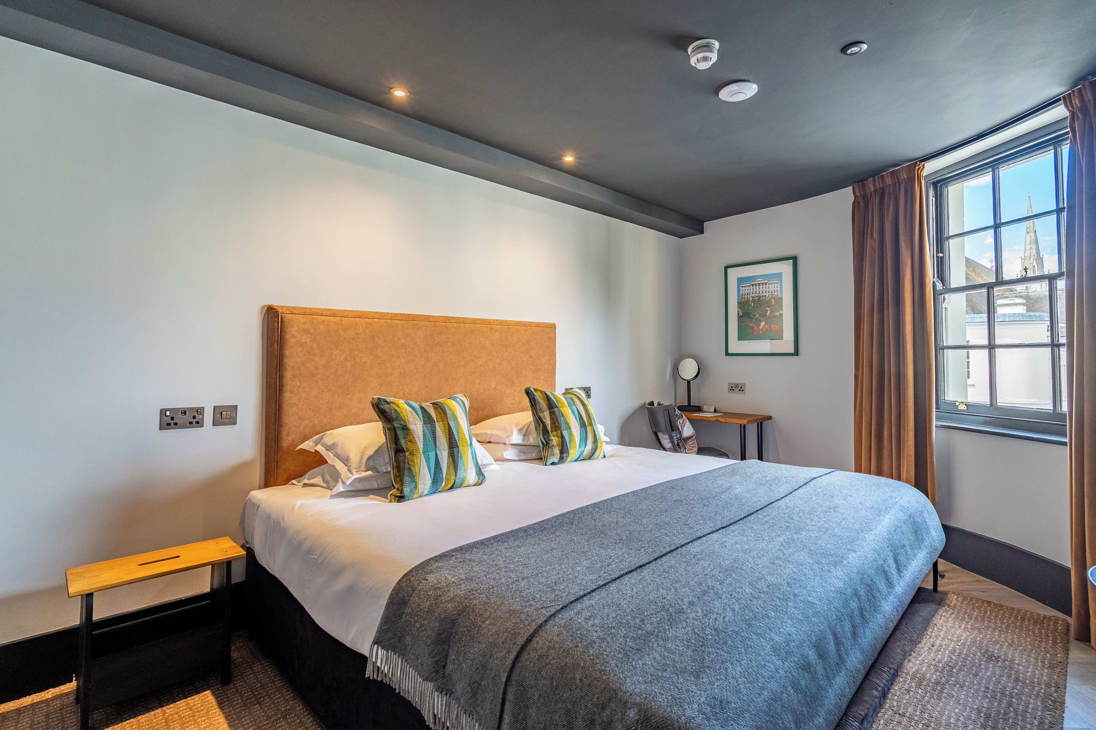 Una habitación de hotel con una cama grande, una mesita de noche, una ventana con cortinas y un cuadro en la pared.