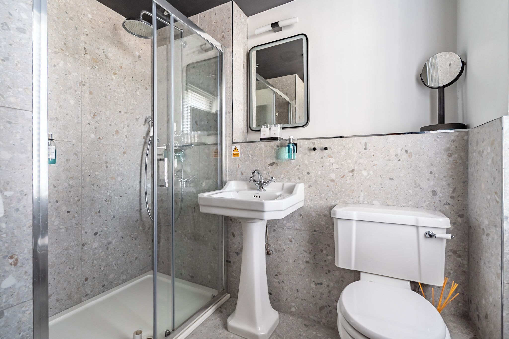 Un baño moderno con ducha de vidrio, lavamanos pedestal y retrete.