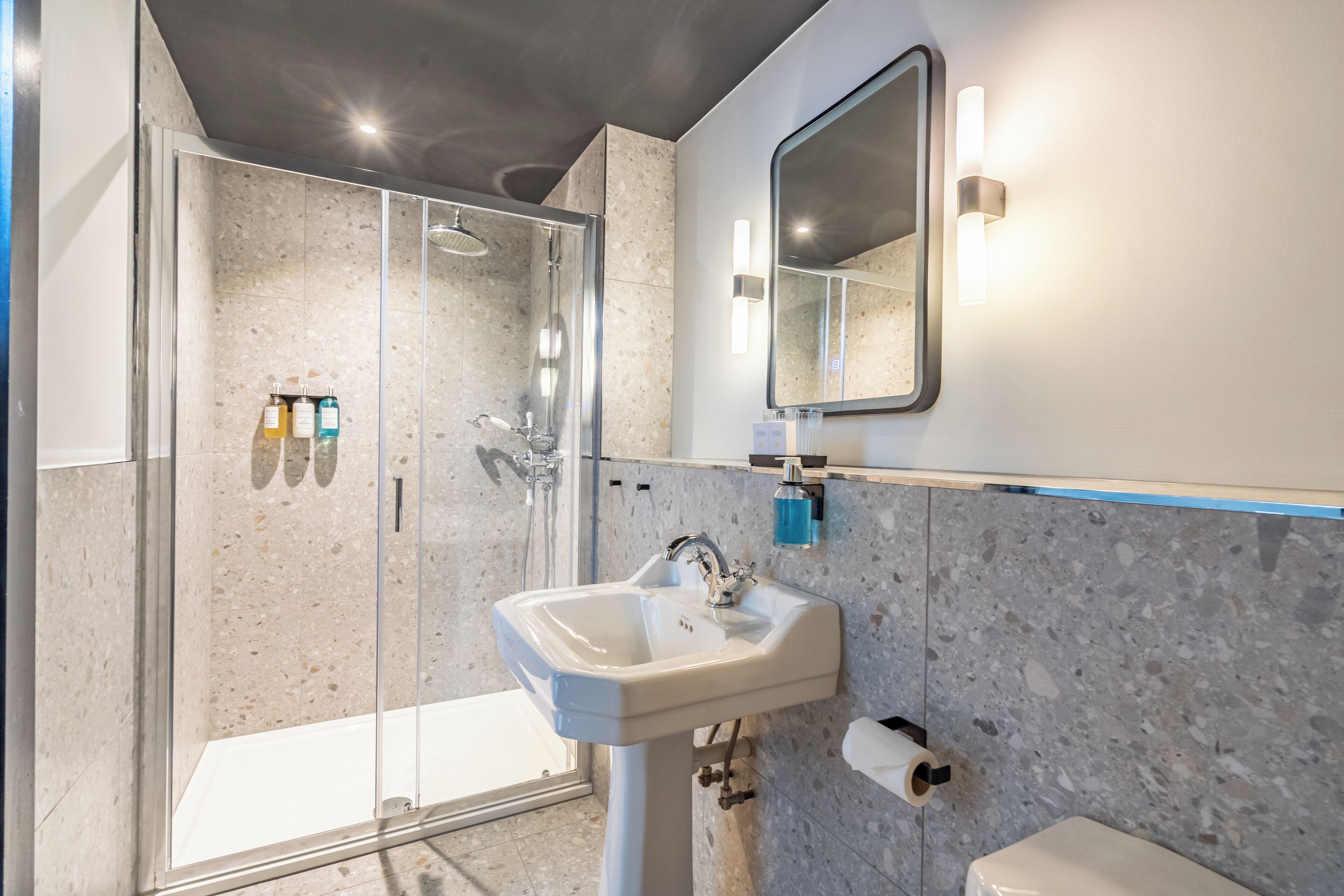 A modern bathroom with a glass-enclosed shower, a pedestal sink, and a large mirror.