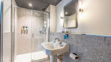A modern bathroom with a glass-enclosed shower, a pedestal sink, and a large mirror.